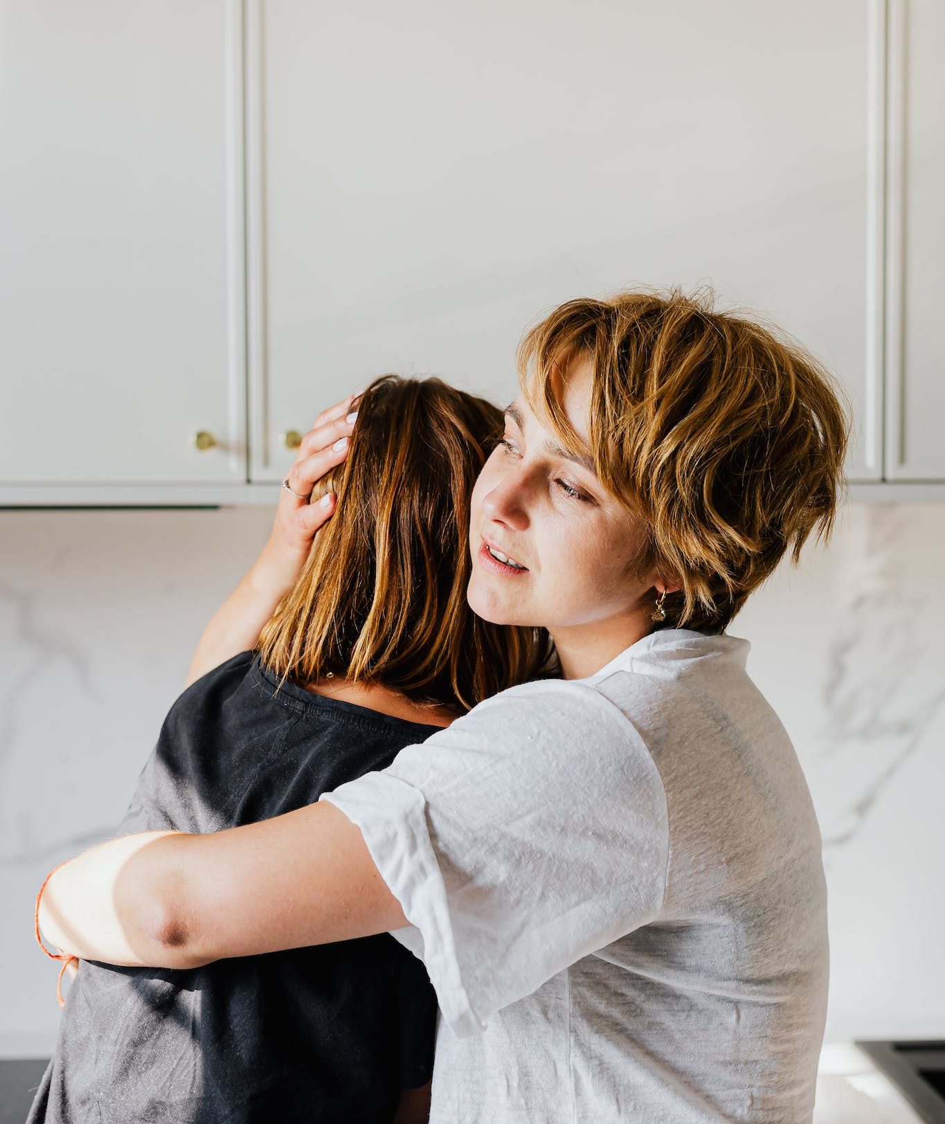 A Woman in White Shirt Embracing a Woman in Gray Top.